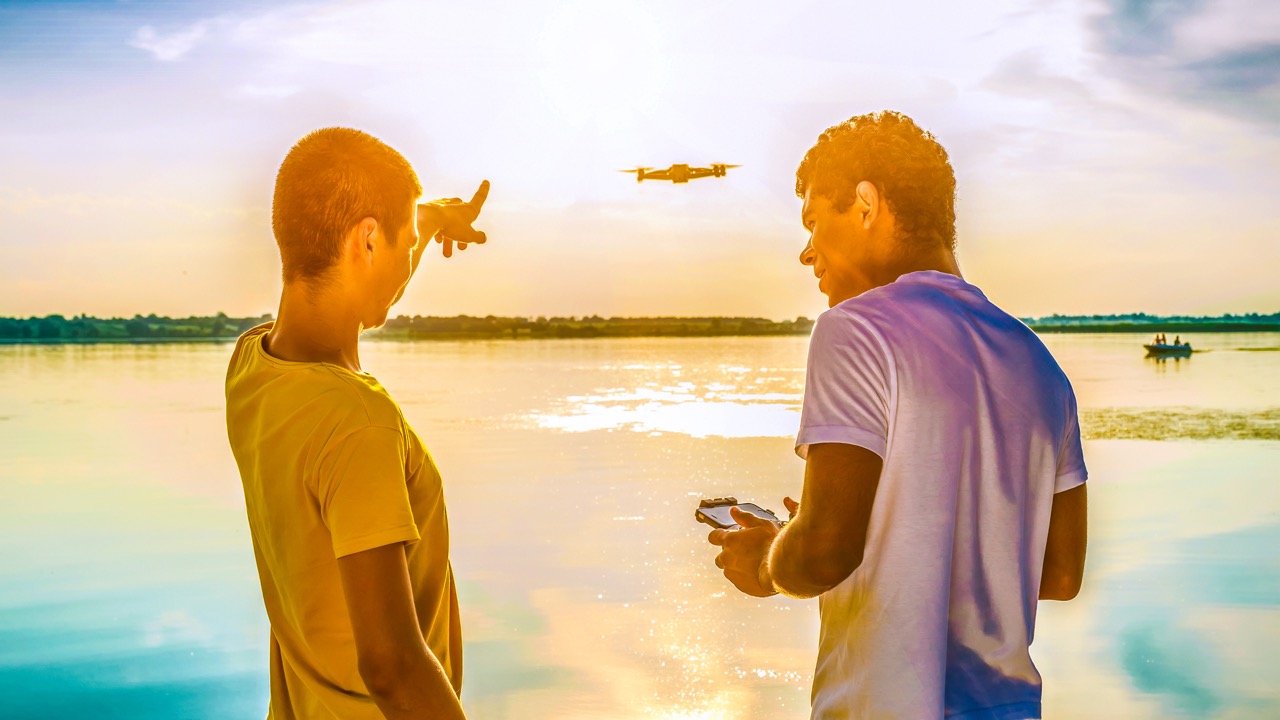 Two friends operating drone with controller standing near the river